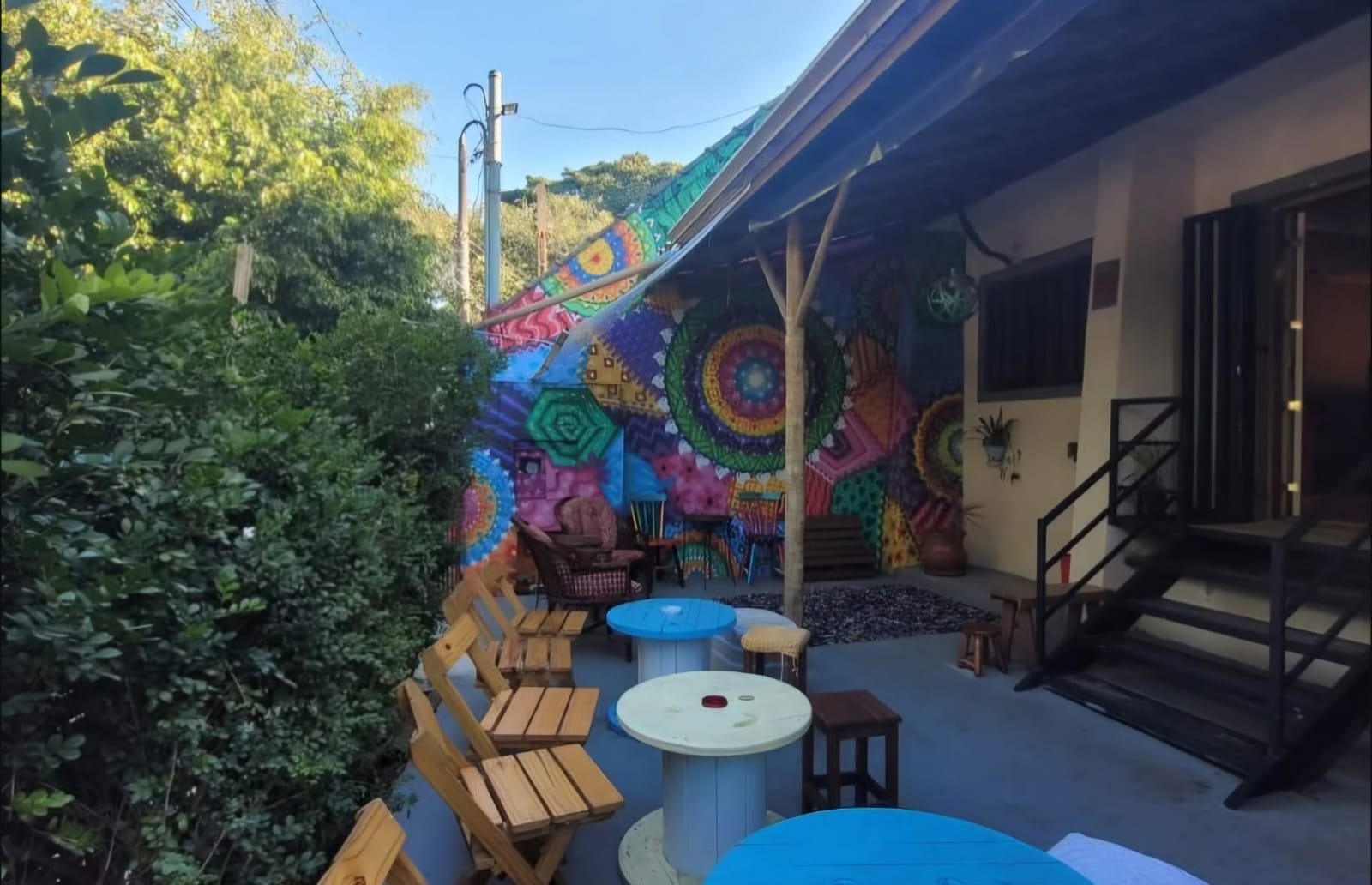 Quintal com mural colorido, mesas de carretel e área verde arborizada